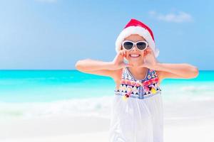 Happy little girl in Santa hat during Christmas beach vacation have a lot of fun photo