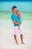 papá joven y su pequeña hija caminando en la playa tropical de arena blanca foto