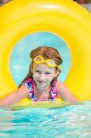 Little girl with inflatable rubber circle having fun in outdoor swimming pool