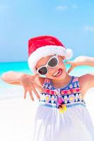 Happy funny little girl in Santa hat during Christmas beach vacation have a lot of fun photo