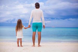 Back view of little girl hugging with dad on the beach photo