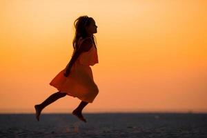 Silhouette of adorable little girl on white beach at sunset photo