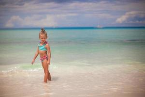 adorable niña caminando en el agua en vacaciones en la playa tropical foto