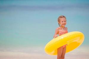 Adorable girl with inflatable rubber circle on white beach ready for swimming photo