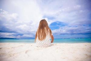 vista trasera de una niña linda sentada en la playa foto