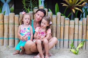 Young mother and two beautiful daughters sitting on the sand near the fence photo