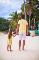 Back view of father with his adorable daughter walking on tropical beach vacation photo