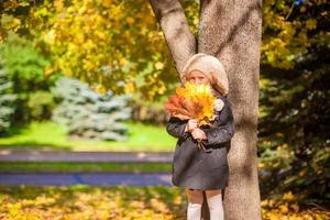 Adorable Fashion girl standing under a tree with bouquet of maple leaves on sunny autumn day photo