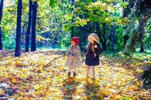 Two beautiful adorable girls walking in the fall forest at warm sunny autumn day photo