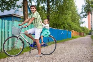 el joven papá rueda a su dulce y encantadora hija en una bicicleta en el campo foto