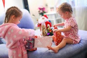 Two charming little sisters early in the morning opening Christmas gifts photo