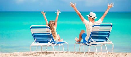 Panorama of family of dad and kid hands up on beach sitting on chaise-longue photo