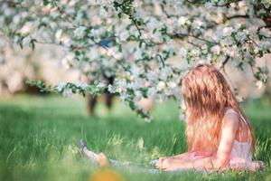 Adorable little girl in blooming cherry tree garden on spring day photo