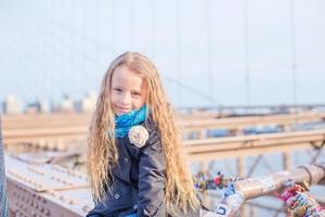 Adorable little girl sitting at Brooklyn Bridge with view on the road photo