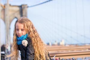 Adorable little girl sitting at Brooklyn Bridge with view on the road photo