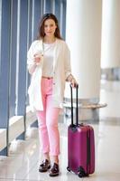 Young woman in international airport walking with her luggage and coffee to go photo