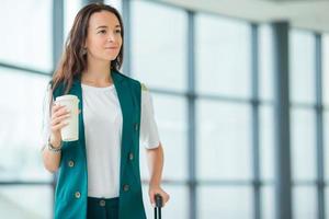 Young woman in international airport walking with her luggage and coffee to go photo