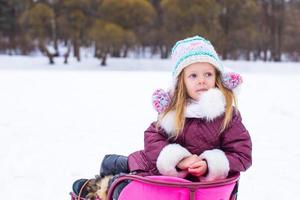 Adorable little happy girl sledding in winter snowy day photo