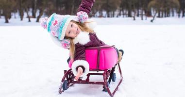 Adorable little happy girl sledding in winter snowy day photo