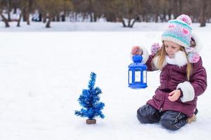 adorable niña sosteniendo linterna de navidad al aire libre en un hermoso día de nieve de invierno foto