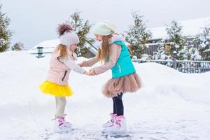 Adorable little girls skating on ice rink outdoors in winter snow day photo