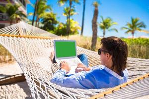 Young man working with laptop in hammock during beach vacation photo