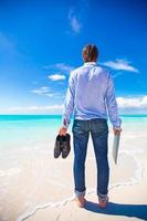 Young man with laptop on the background of turquoise ocean at tropical beach photo