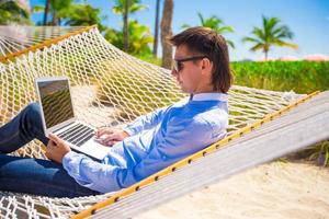 Young man working with laptop in hammock during beach vacation photo