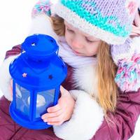 Adorable little girl holding Christmas lantern outdoors on beautiful winter snow day photo