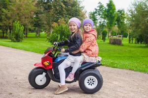 Little adorable sisters sitting on toy motorcycle in green park photo