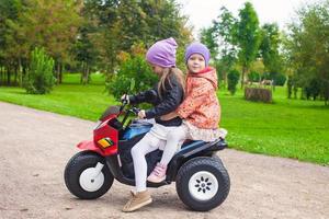 Adorable little girls riding on kid's bike in the green park photo