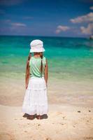 Back view of little girl in hat looking at the sea on white sand beach photo