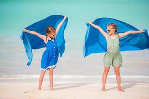 Little girls have fun with beach towel during tropical vacation photo