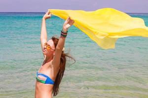 Beautiful young girl holding yellow fabric at wind in beach vacation photo