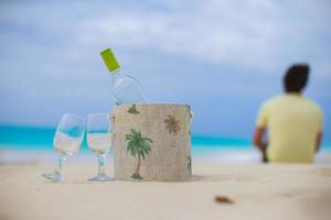 botella de vino blanco y dos copas en la exótica playa de arena foto
