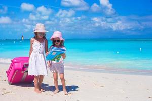 Little girls with big suitcase and map searching for the way on tropical beach photo