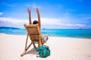 mujer joven relajante en silla de madera playa en vacaciones tropicales foto