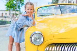 adorable niña en zona popular en la habana vieja, cuba. retrato de niño fondo vintage coche americano clásico foto