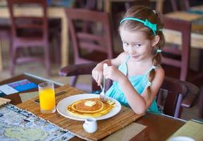 Adorable little girl having breakfast at outdoor cafe photo