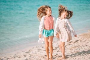 Little happy funny girls have a lot of fun at tropical beach playing together. Sunny day with rain in the sea photo