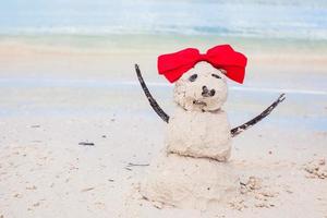 pequeño muñeco de nieve de arena con arco en la playa caribeña blanca foto