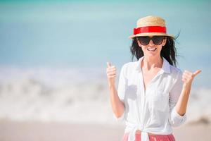 Young woman enjoying the sun sunbathing by perfect turquoise ocean. Girl lifts thumbs up outdoors photo