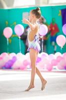 pequeña y hermosa gimnasta en la alfombra. adorable gimnasta participa en competiciones de gimnasia rítmica foto