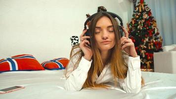 girl listens to music with headphones with a bunch of Christmas gifts on the bed at the new years eve video