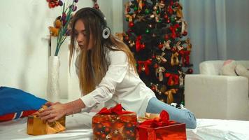 girl listens to music with headphones with a bunch of Christmas gifts on the bed at the new years eve in slow motion video