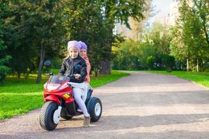 Adorable little girls riding on kid's motobike in the green park photo