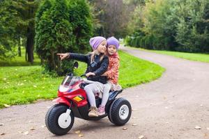 Adorable little girls riding on kid's bike in the green park photo