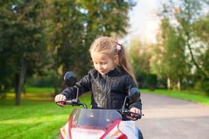 adorable niña feliz con chaqueta de cuero sentada en su motocicleta de juguete foto