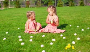 Two adorable little girls having fun with Easter Eggs on green grass photo