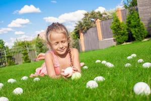 Little happy girl playing with white Easter eggs on green grass photo